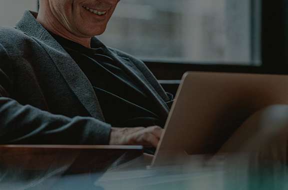A man in a grey blazer is using a laptop.