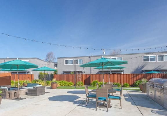 a patio with tables chairs and umbrellas and a grill at The Preston at Hillsdale, San Mateo, CA