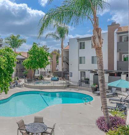 a swimming pool with tables and chairs and palm trees at City View Apartments at Warner Center, Woodland Hills, CA