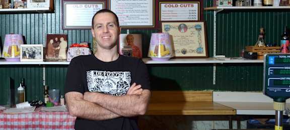 A man in a black shirt is standing in front of a counter with his arms crossed.
