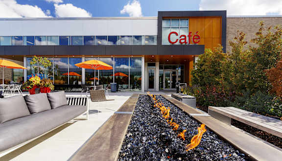 A cafe with a white and orange signboard and a long wooden bench in front of it.