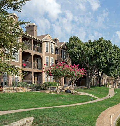 A large building with a balcony is surrounded by a grassy area and a body of water.