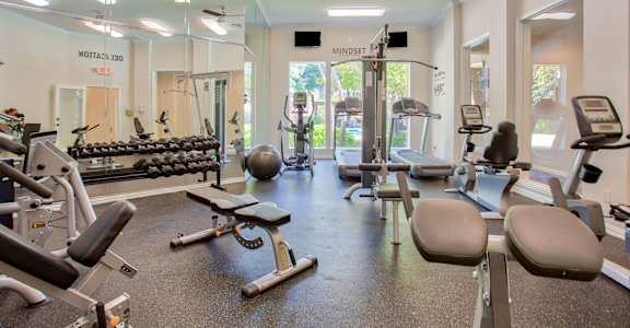A gym with a variety of equipment including weights, machines, and a bench.