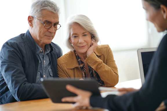 Three people are sitting at a table looking at a tablet.