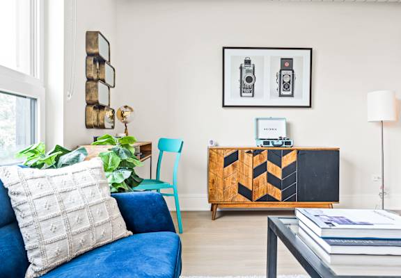 A blue couch with a white pillow and a wooden cabinet with a blackboard on it.