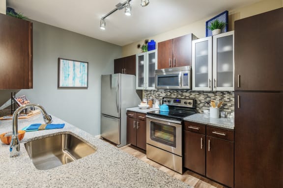 Nona Park Village Apartments pool area gourmet kitchens with tile backsplash, granite countertops, custom cabinetry, and stainless steel appliances
