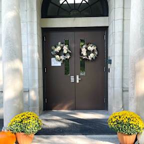A brown door with a flower wreath and two pumpkins in front of it.