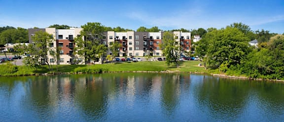 Lakeside view of Panton Mill Apartments with modern buildings, green trees, and water on a sunny day in Illinois