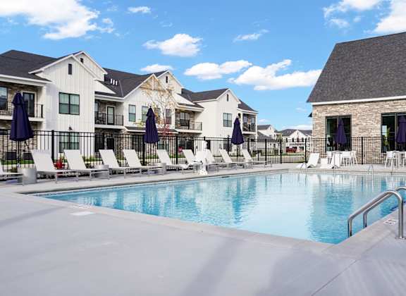 A swimming pool surrounded by lounge chairs and umbrellas in front of a building.