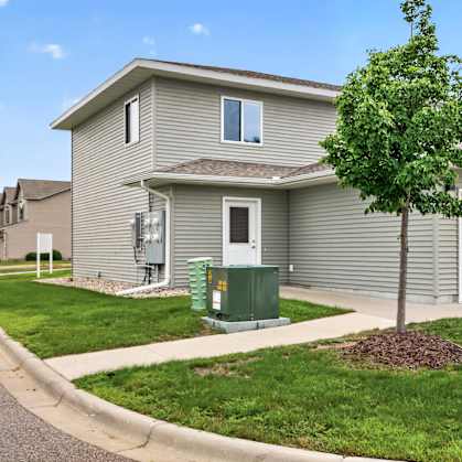 A tree in front of a grey house with a green utility box.