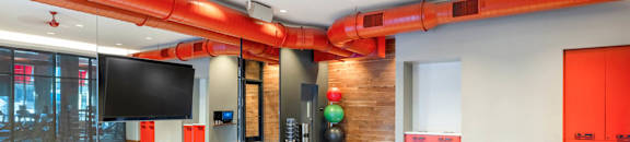 A room with wooden floors and red pipes on the ceiling.