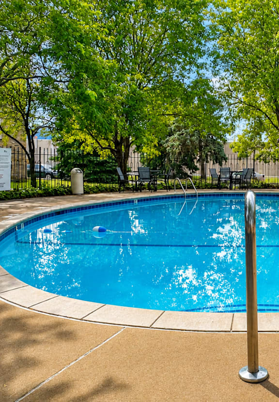 A round blue pool surrounded by trees and chairs.
