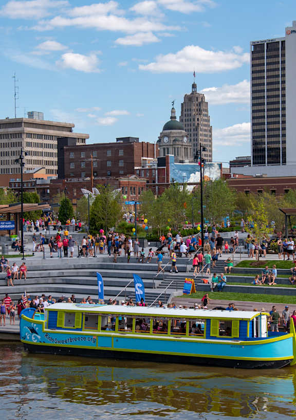 A blue boat is on a river in a city with tall buildings.