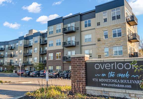 The image shows a multi-story residential building with a sign in front that reads