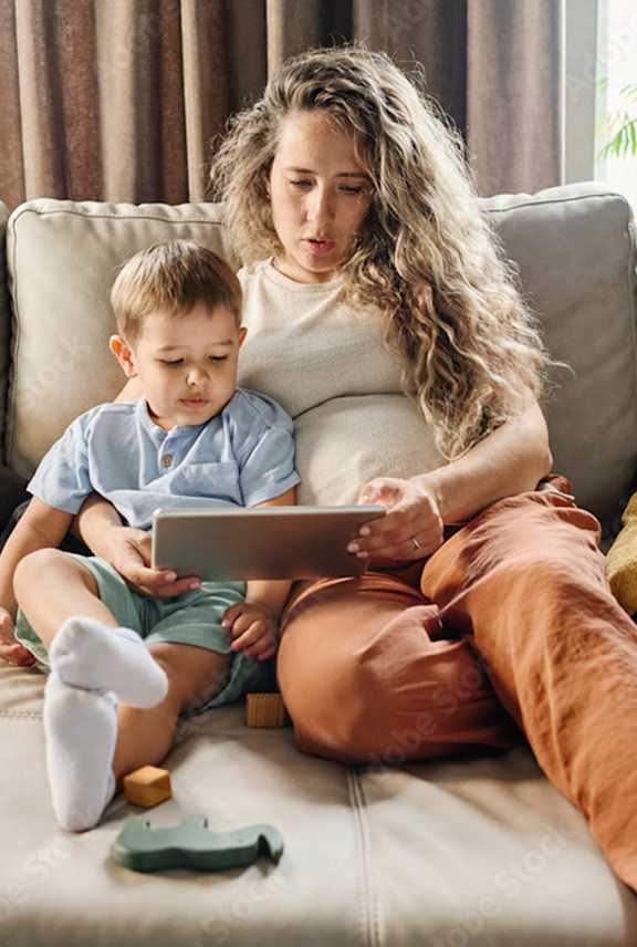 A woman and a child are sitting on a couch with a tablet. at Grand Manor Apartments , Grand Junction
