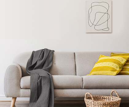 A grey couch with a grey throw and a yellow pillow on it.