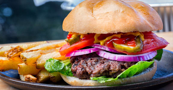 A burger with lettuce, tomato, onion, and pickles on a bun.