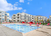 Thumbnail 24 of 30 - A swimming pool surrounded by red chairs and buildings in the background.