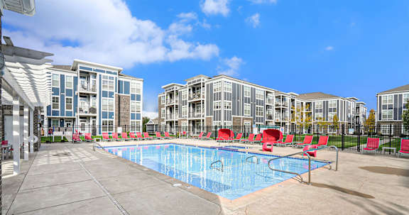 A swimming pool surrounded by red chairs and buildings in the background.