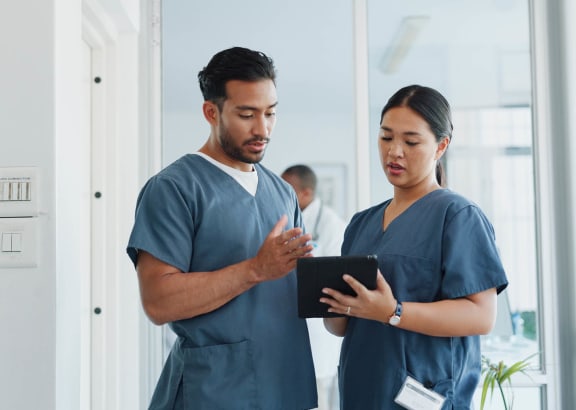 a man and a woman in blue scrubs look at a tablet