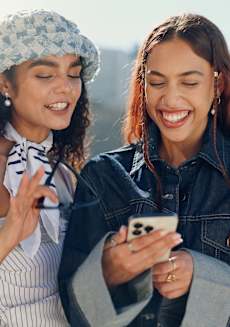 Two women are standing outside, one is showing something on her phone to the other.
