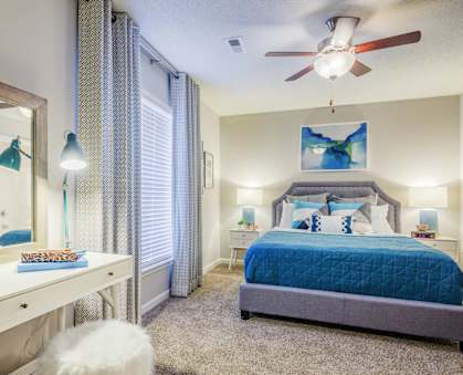 A bedroom with a blue bedspread and a white dresser with a mirror.