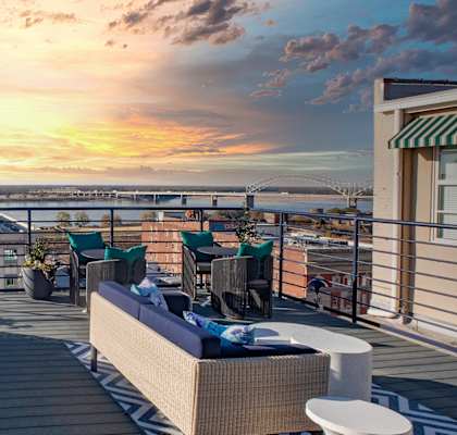 a rooftop deck with furniture and a sunset over the ocean