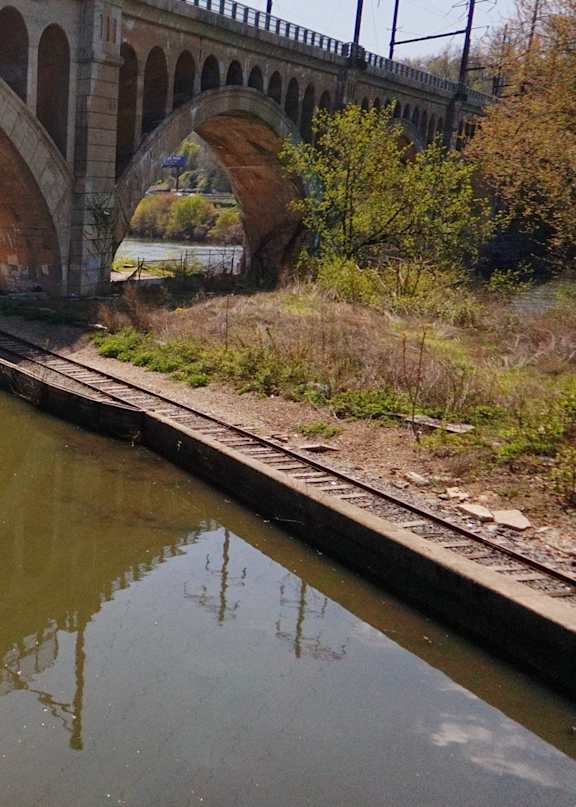 A bridge over a calm river with a wooden walkway on the left.