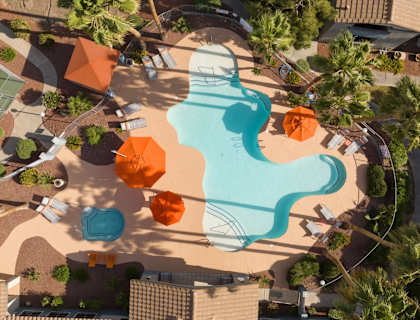 An aerial view of a pool surrounded by orange umbrellas and palm trees.