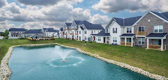 a fountain in the middle of a pond in front of houses