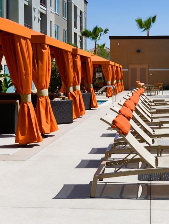 A Row of Chaise Lounges are lined up next to a Sparkling  Blue Swimming Pool with cabanas in the Background at Circa 2020 in Redlands, 92374