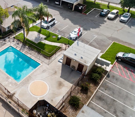 An aerial view of a swimming pool surrounded by a fence and a parking lot.