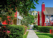 Thumbnail 42 of 60 - Fusion Orlando apartments pathway lined with lush landscaping and two story apartment buildings with red chimneys and outdoor stairs.
