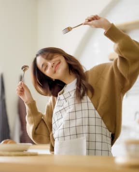 Woman Smiling while Holding Silverware in Kitchen