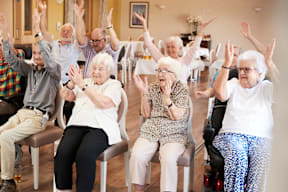 A group of elderly people are sitting in a room and raising their hands in the air.