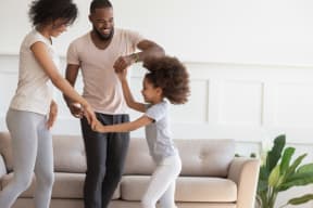 a young girl dances with her parents in a living room