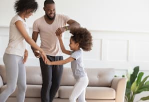 A family of three is dancing together in a living room.