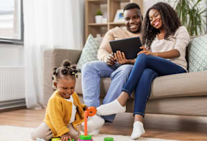 A family of three is sitting on a couch with a tablet in their hands.