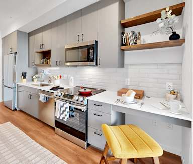 A modern kitchen with a yellow chair and white cabinets.