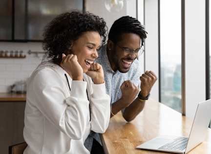 Two people celebrating in front of a laptop.