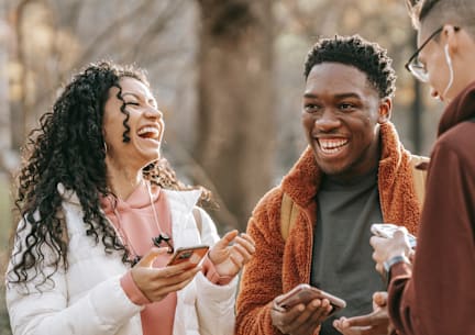 Three people are standing outdoors, looking at their smartphones.