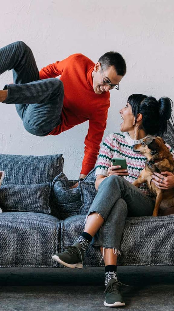 a man jumping over a couch with a woman and a dog