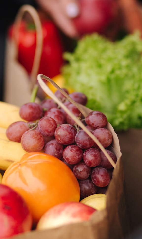 A bunch of bananas, grapes, apples, and lettuce are tied together in a paper bag.