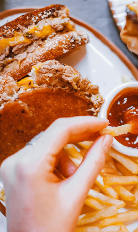 A person is eating a sandwich with fries and ketchup.