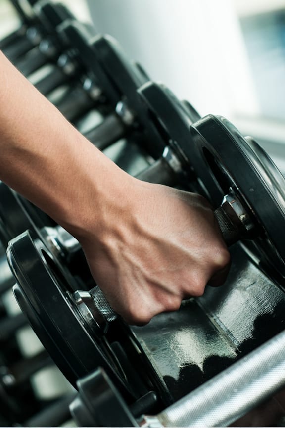 A person's hand is lifting a dumbbell in a gym.