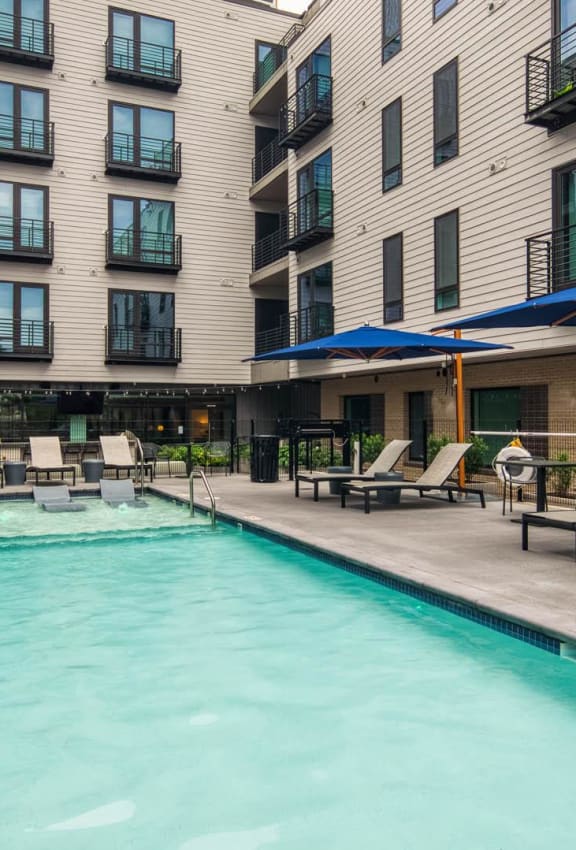 a swimming pool with chairs and umbrellas in front of an apartment building