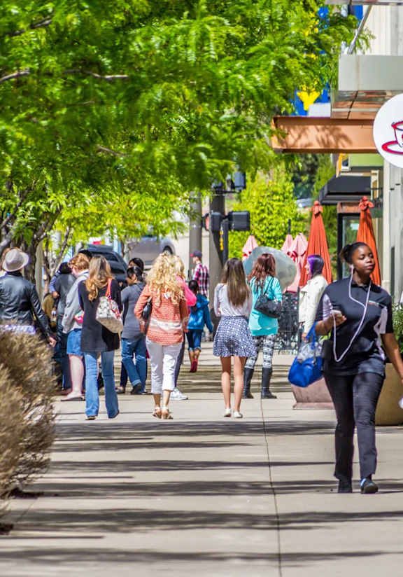 A street scene with people walking and trees lining the sidewalk.