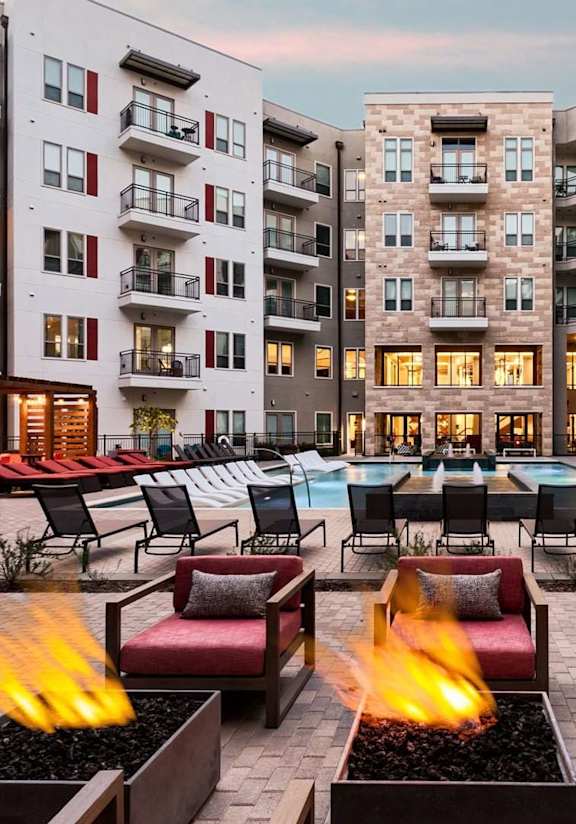 A fire pit in the middle of a courtyard surrounded by chairs and buildings.