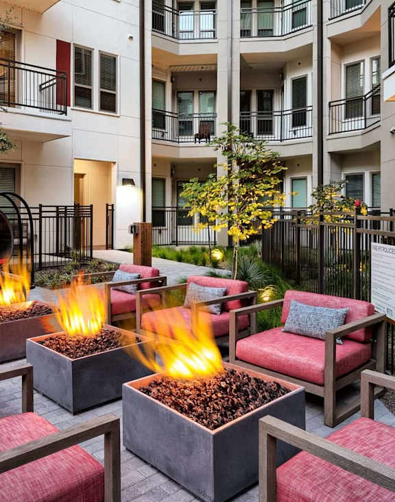 A patio with red cushioned chairs and a fire pit.