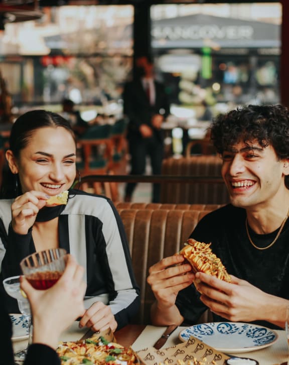 three people sitting at a table eating pizza in a restaurant